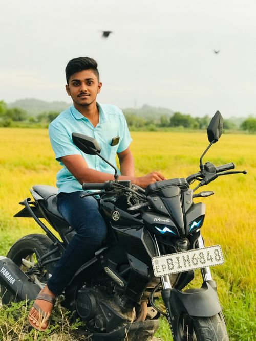 Free A young man seated on a black motorcycle in a lush countryside setting. Stock Photo