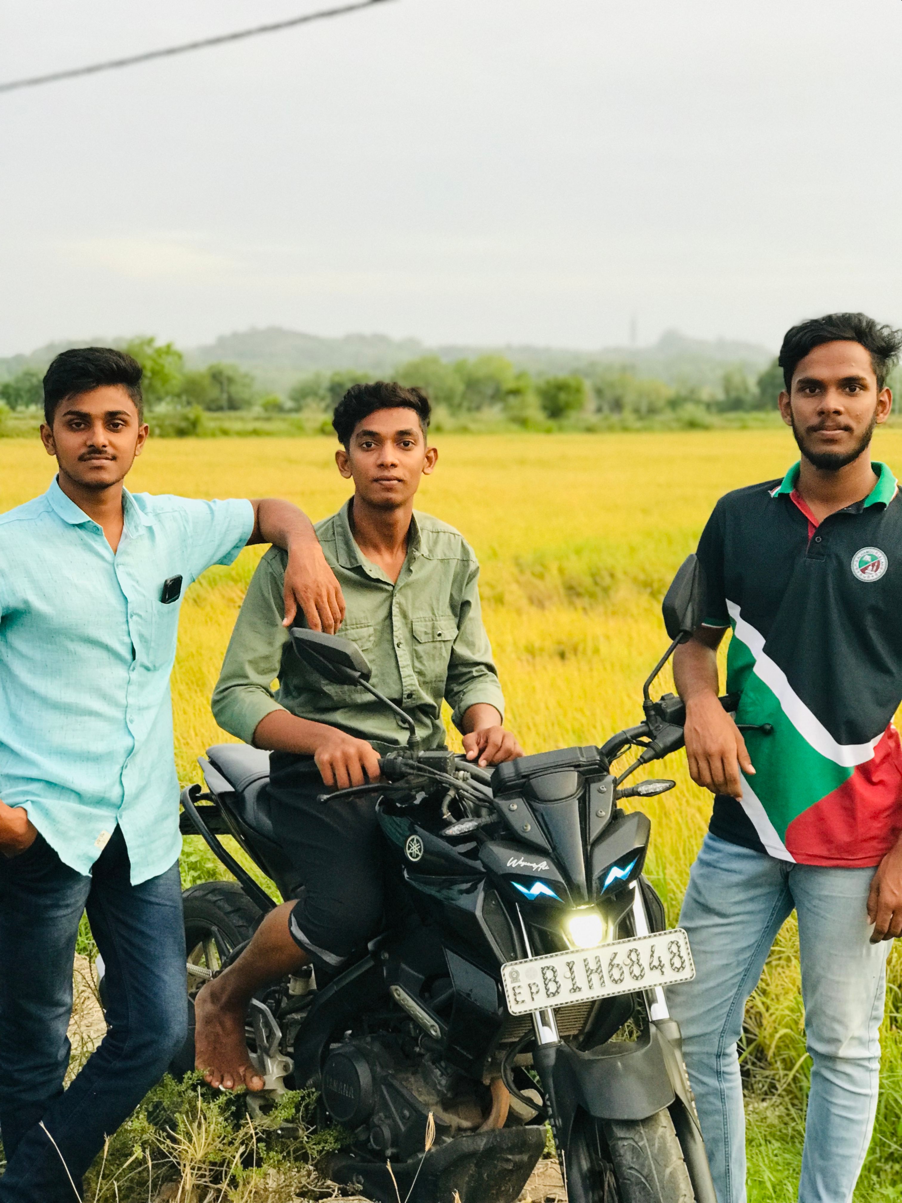Three young men enjoying an outdoor adventure with a motorcycle in a lush field.