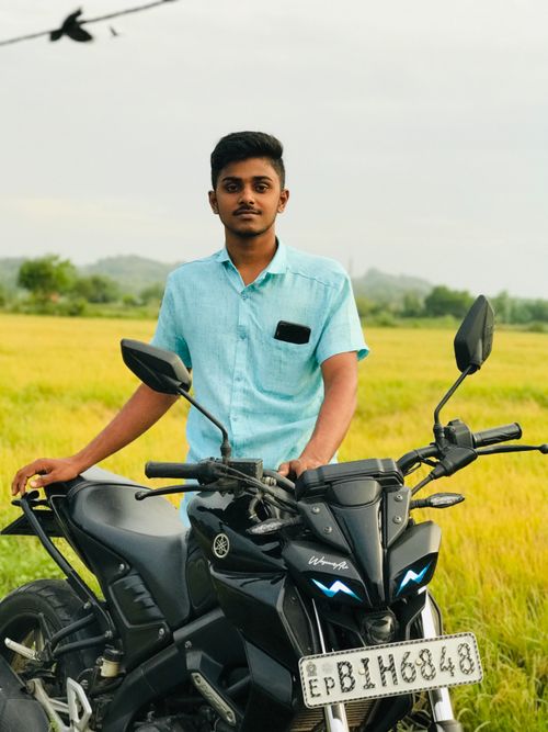 Free A young man stands by his motorcycle in a scenic field, exuding adventure and freedom. Stock Photo