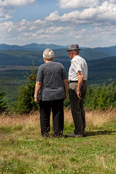 Elderly couple enjoys a serene view of distant mountains under a clear sky.