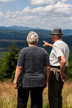 Senior couple standing together, admiring a stunning mountain landscape on a sunny day.