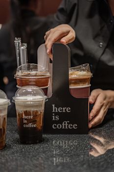 Close-up of hands serving iced coffee in takeaway carrier at a cafe.