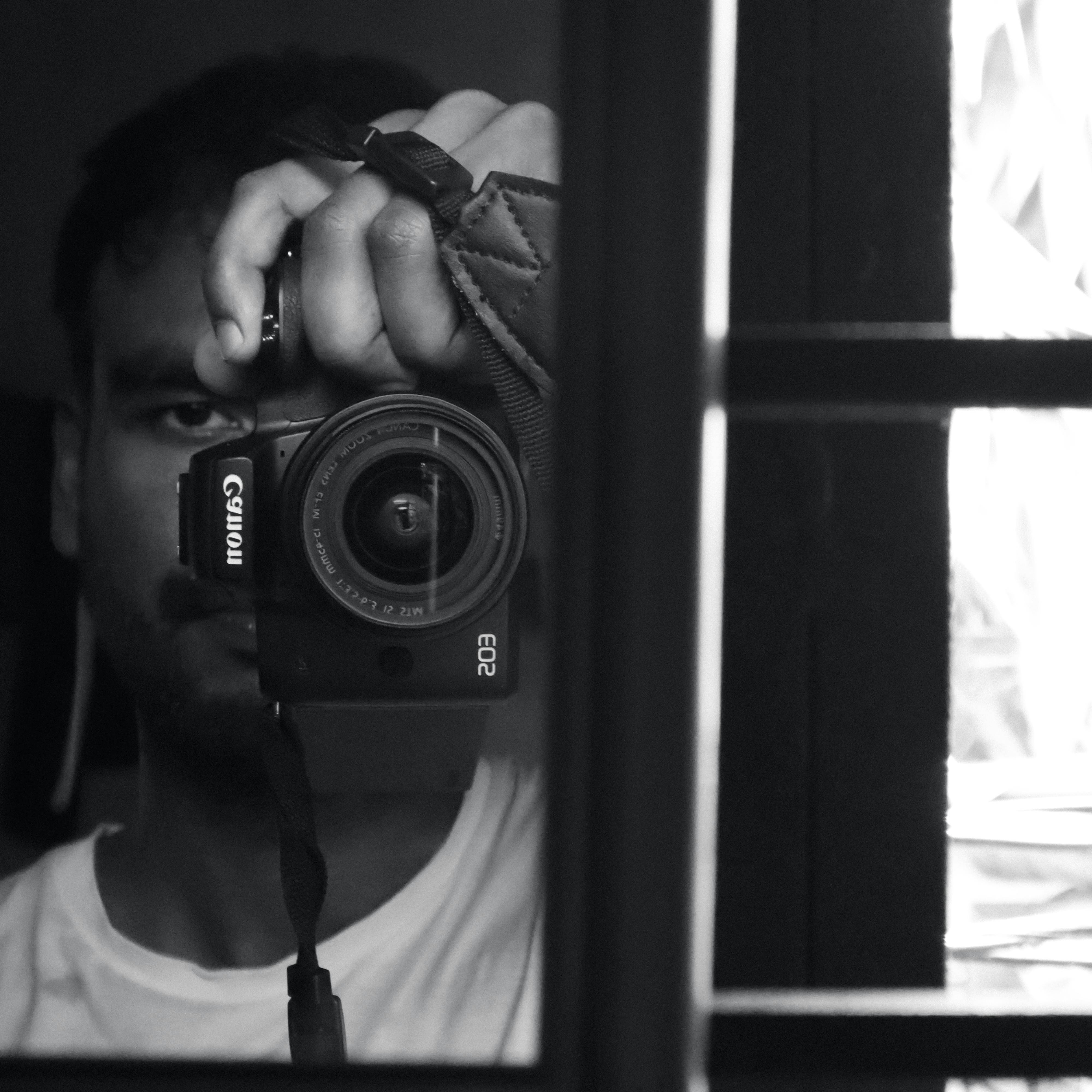 Monochrome self-portrait with camera reflected in a mirror.