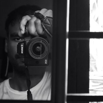 Monochrome self-portrait with camera reflected in a mirror.
