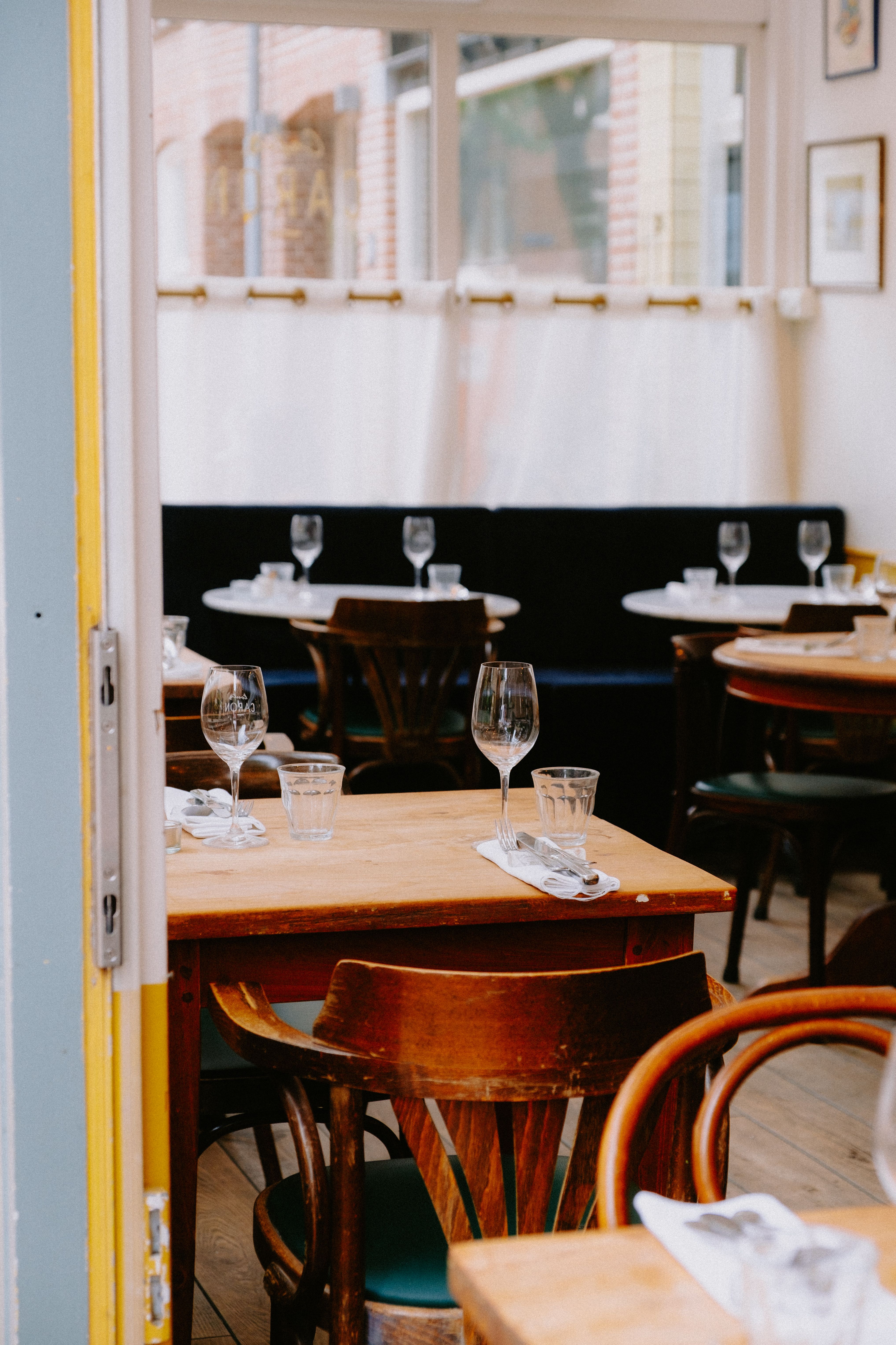 Inviting restaurant interior with wooden tables set for dining, featuring elegant glassware and natural light.