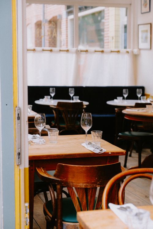 Free Inviting restaurant interior with wooden tables set for dining, featuring elegant glassware and natural light. Stock Photo