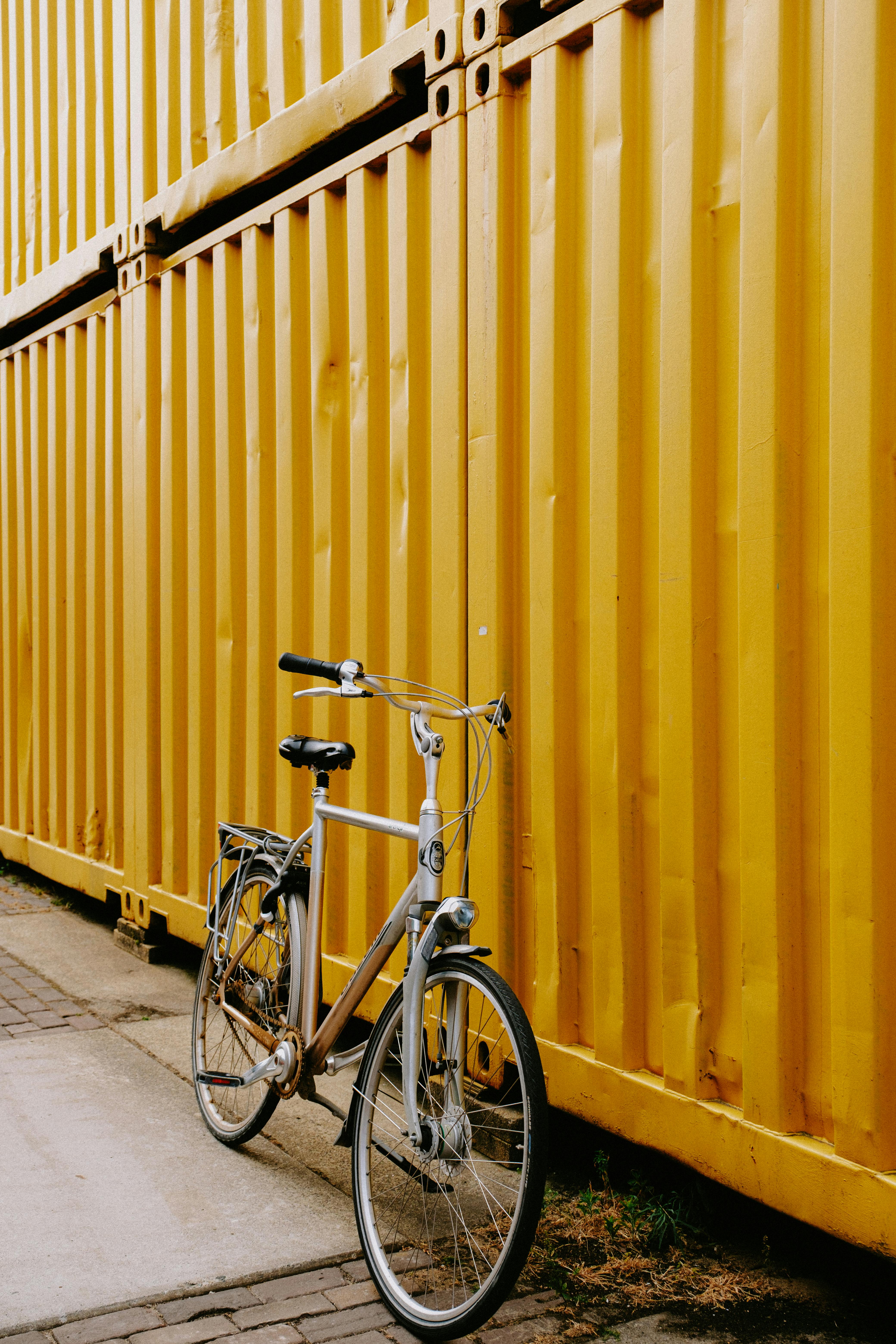 Retro bicycle leaning against vibrant yellow container wall in urban setting.