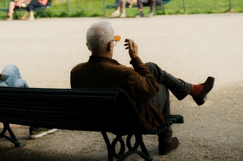 Free Senior man sitting on a park bench enjoying a sunny day outdoors. Stock Photo