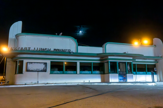 Vintage diner facade lit by streetlights and moonlight at night, exuding nostalgic charm.
