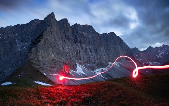 Mysterious alpine mountain scene with striking red light trail at dusk.