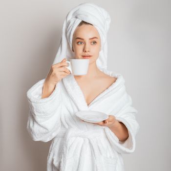 Young woman in a white bathrobe sipping morning coffee, embracing relaxation.