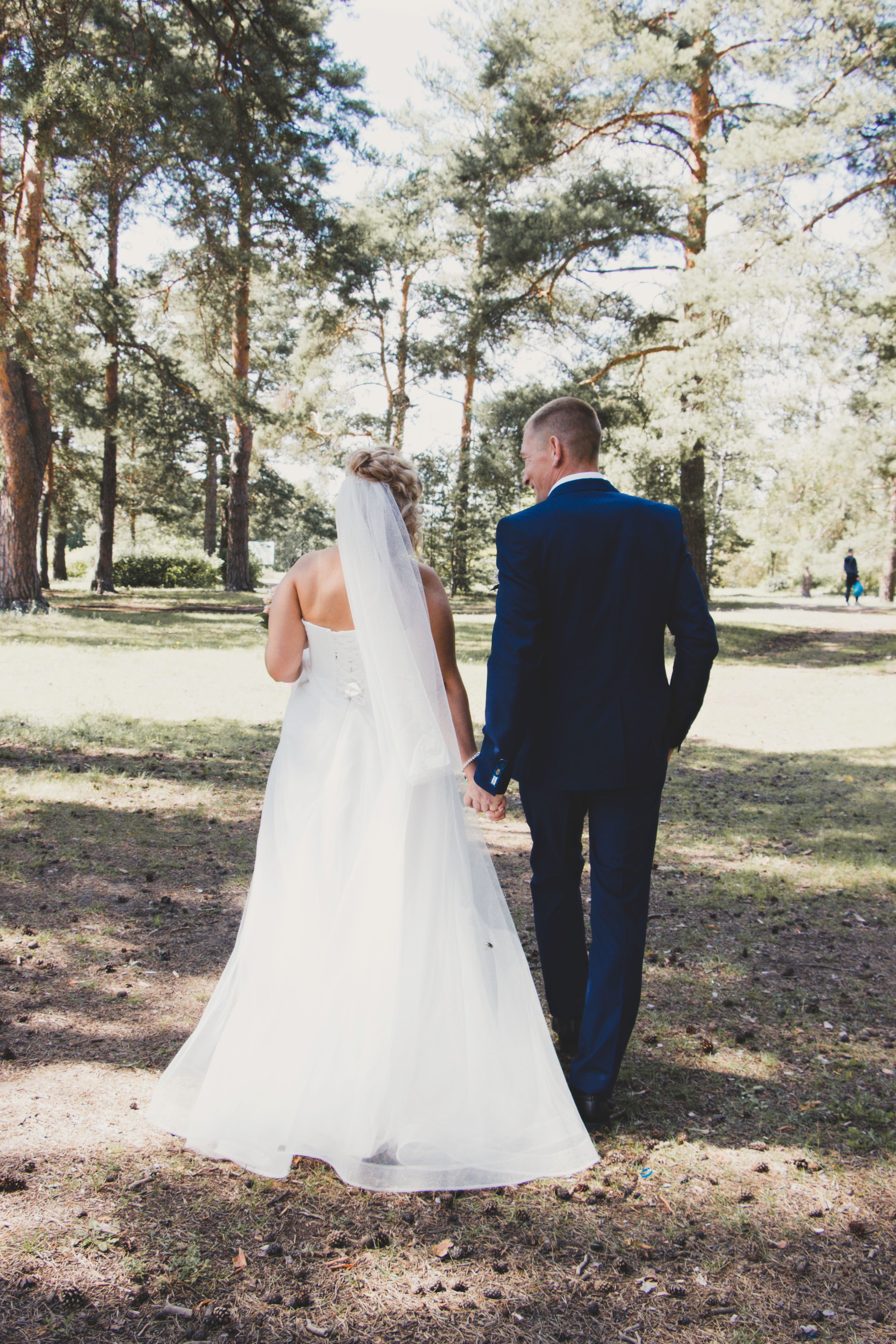 A bride and groom walking through the woods · Free Stock Photo