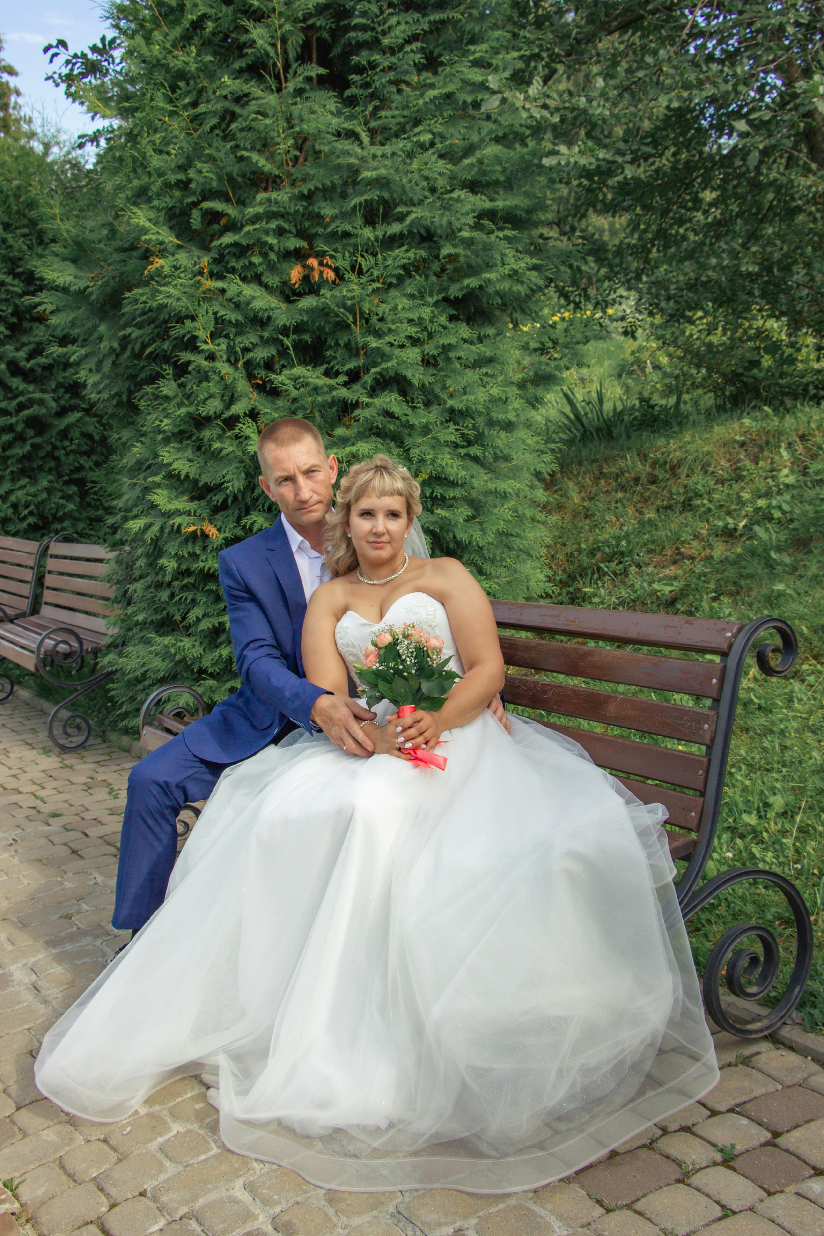 a bride and groom sitting on a bench in a park