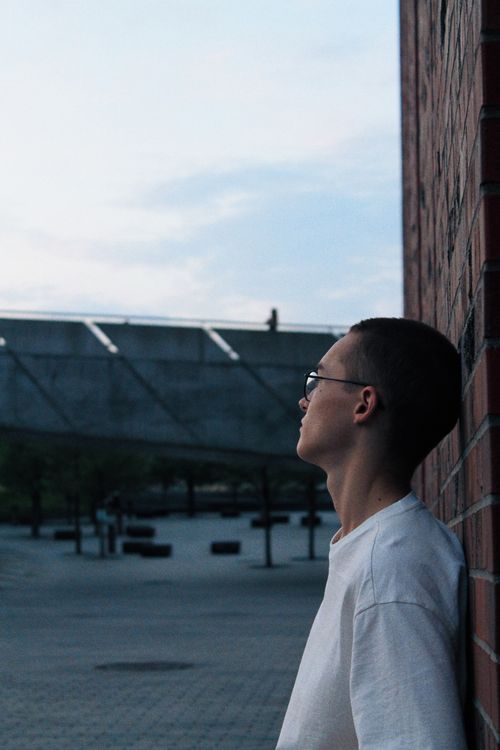 Free Contemplative young adult leaning against a brick wall in Katowice, Poland. Stock Photo