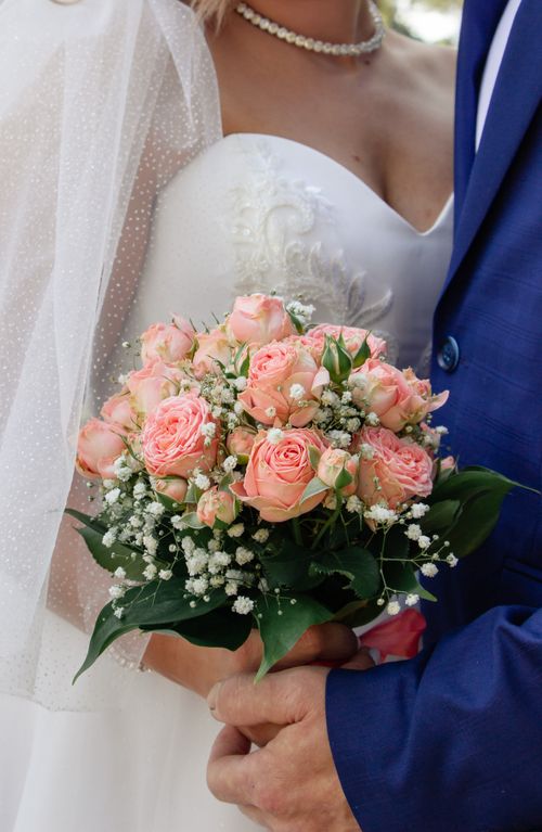 Free A romantic wedding scene featuring a bride holding a pink rose bouquet, alongside the groom in a blue suit. Stock Photo