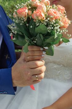 Close-up of a bride and groom holding a bouquet during an outdoor wedding ceremony.