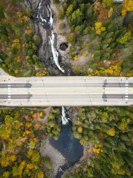 Aerial shot capturing a bridge over a vibrant autumn forest and river.