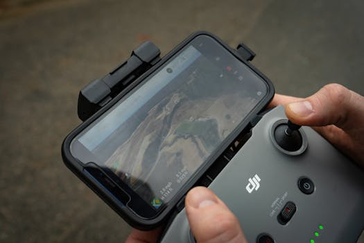 Hands controlling a drone with a smartphone display showing aerial view, demonstrating modern technology use.