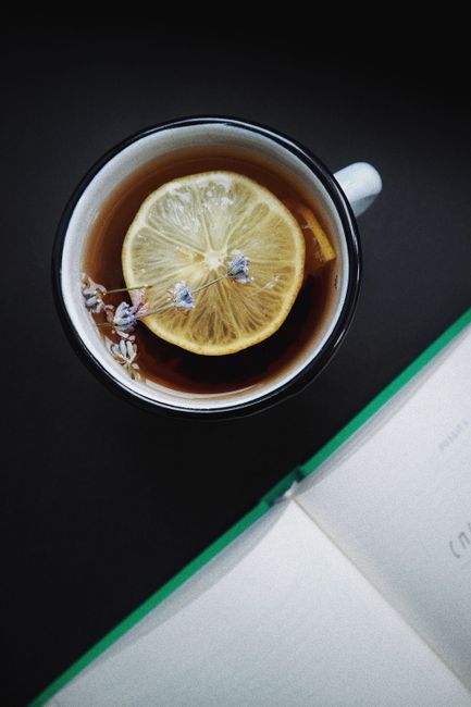 A close-up view of a lemon herbal tea with lavender flowers and an open book in the background. Perfect cozy moment indoors.