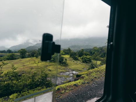 Lush green landscape seen through a vehicle window on a foggy day, offering a tranquil view.