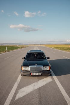 A classic black Mercedes cruising down an open highway under a clear sky.