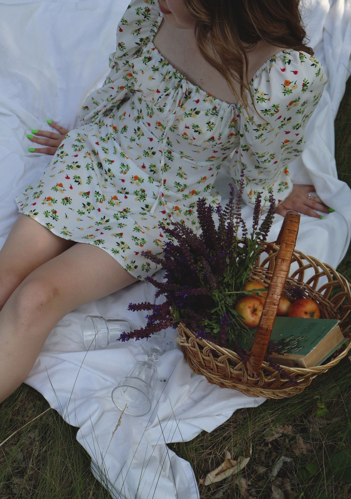 A woman in a floral dress sitting on a blanket with a basket of fruit — the unhurried summer mood