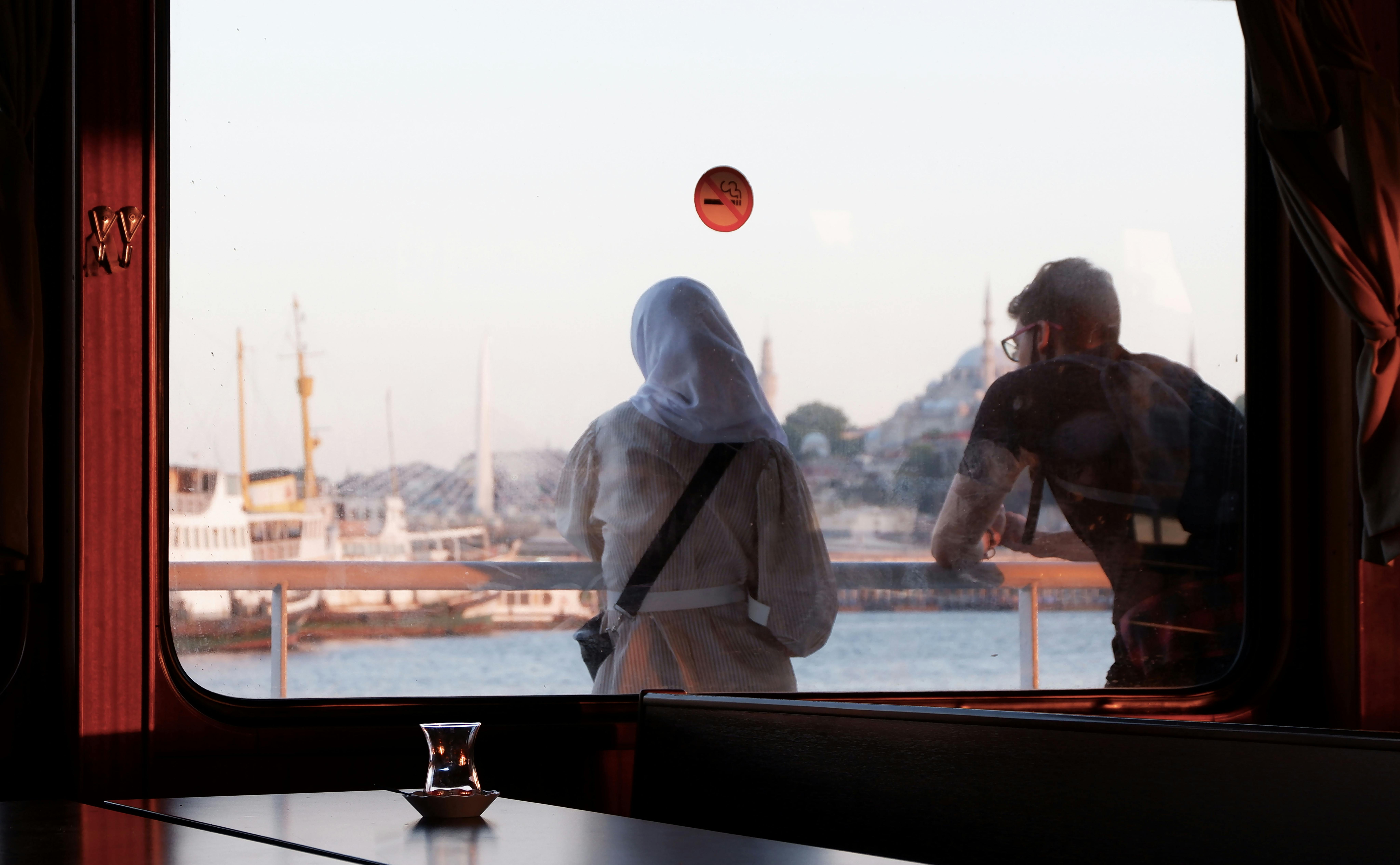 Two people enjoy a scenic sunset view from a ferry in Istanbul, overlooking iconic architecture.