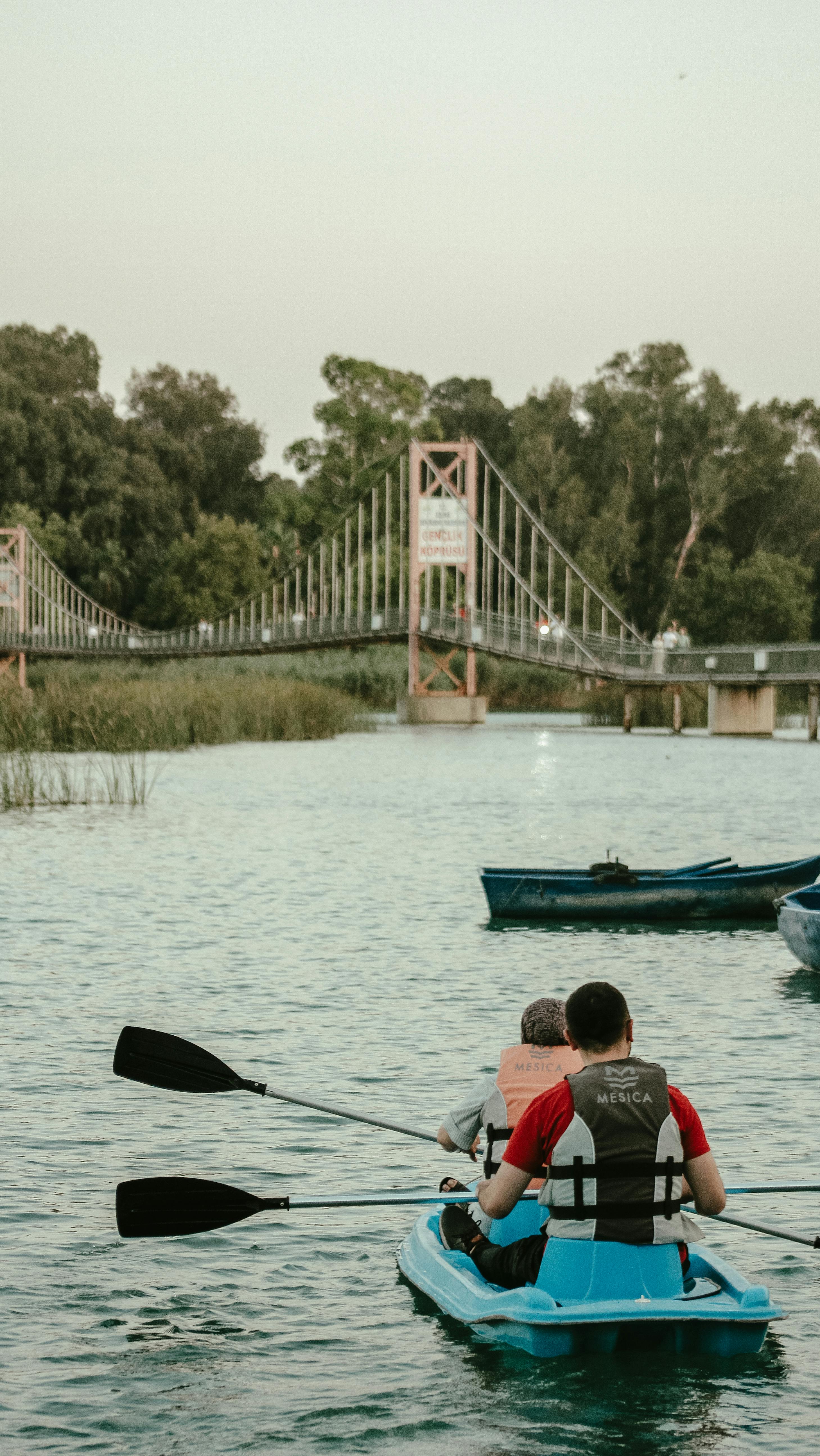 two people in kayaks on the water near a bridge