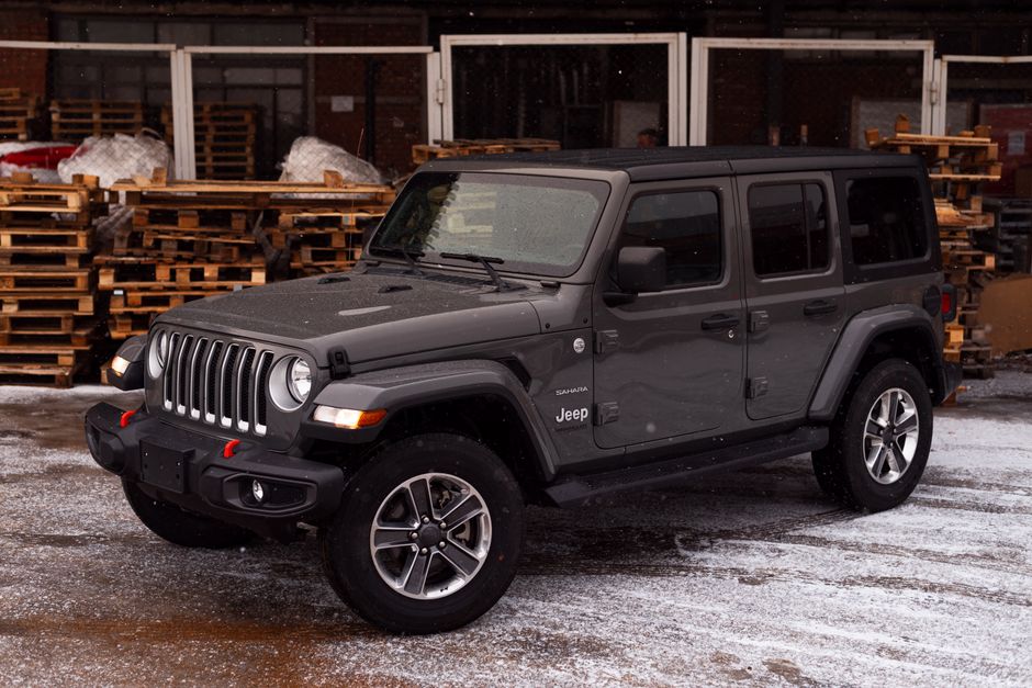 A gray Jeep Wrangler parked outdoors on a snowy ground surrounded by wooden pallets.