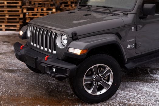 A detailed view of the front part of a Jeep Sahara parked in a snowy area with wooden pallets in the background.