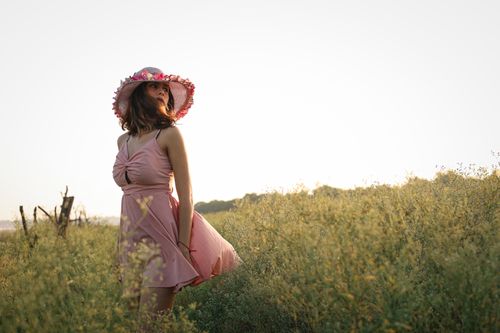 Free A woman in a pink dress and hat stands gracefully in a sunlit field, embracing nature. Stock Photo