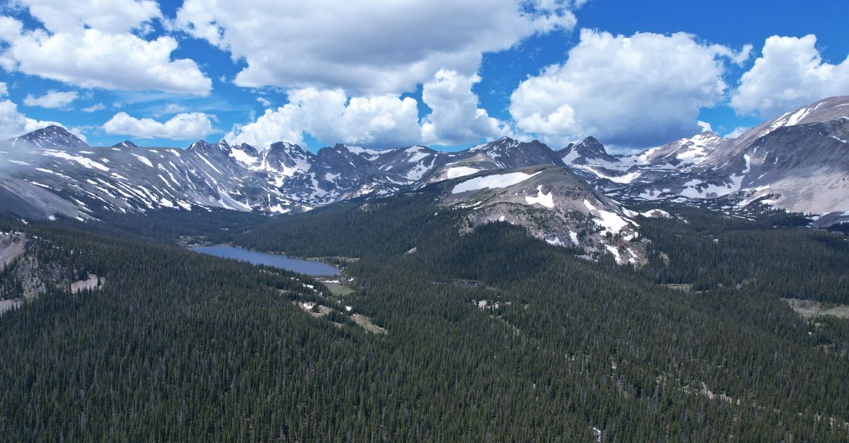 A breathtaking view of the Rocky Mountains in Colorado with lush forests and snow-capped peaks under a blue sky.