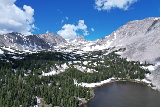 Stunning winter aerial view of snow-capped mountains, forest, and a lake in Colorado Springs.