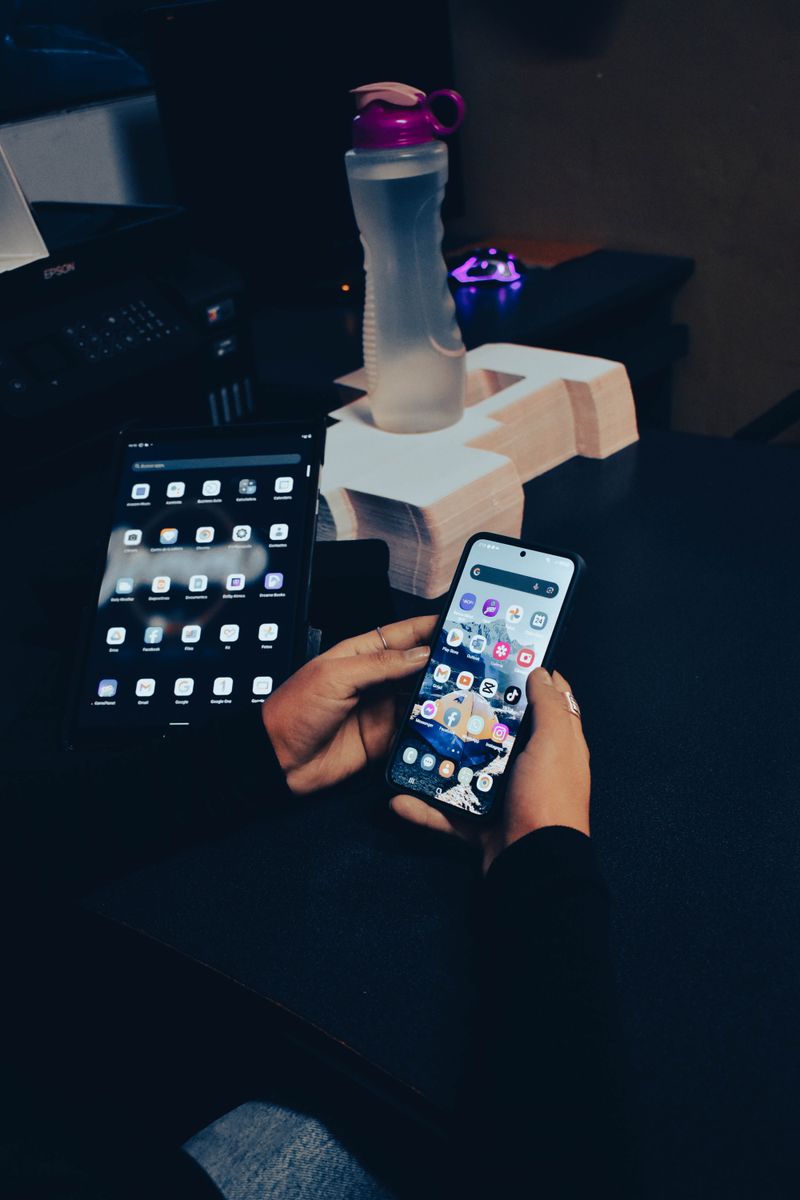 A person multitasking with a smartphone and tablet on a desk, showcasing modern technology usage.