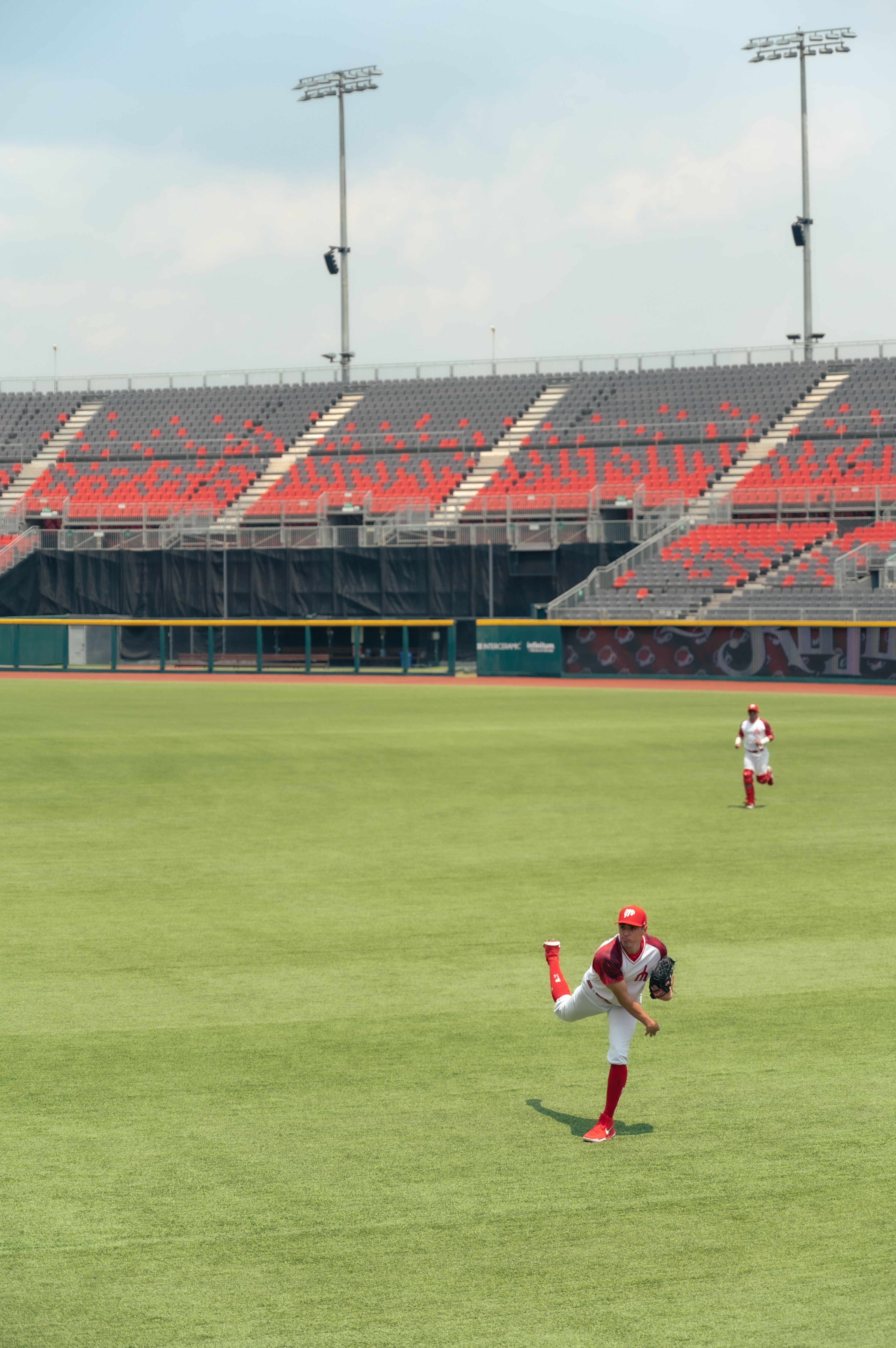 Two baseball players in uniform practice on a sunny day in an empty stadium.
