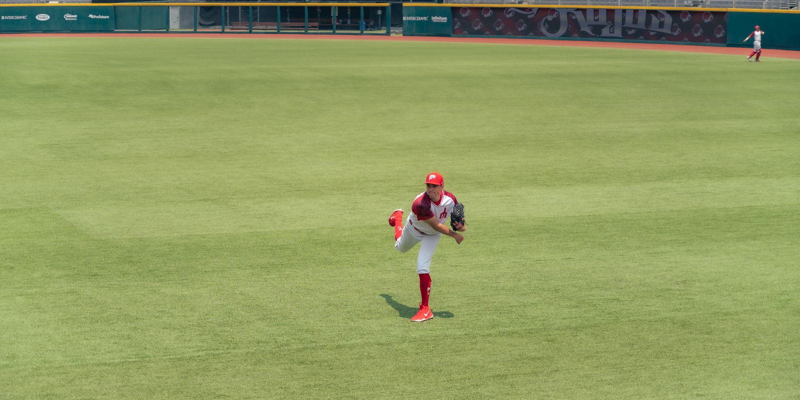 Baseball player pitching on a grass field in a small stadium