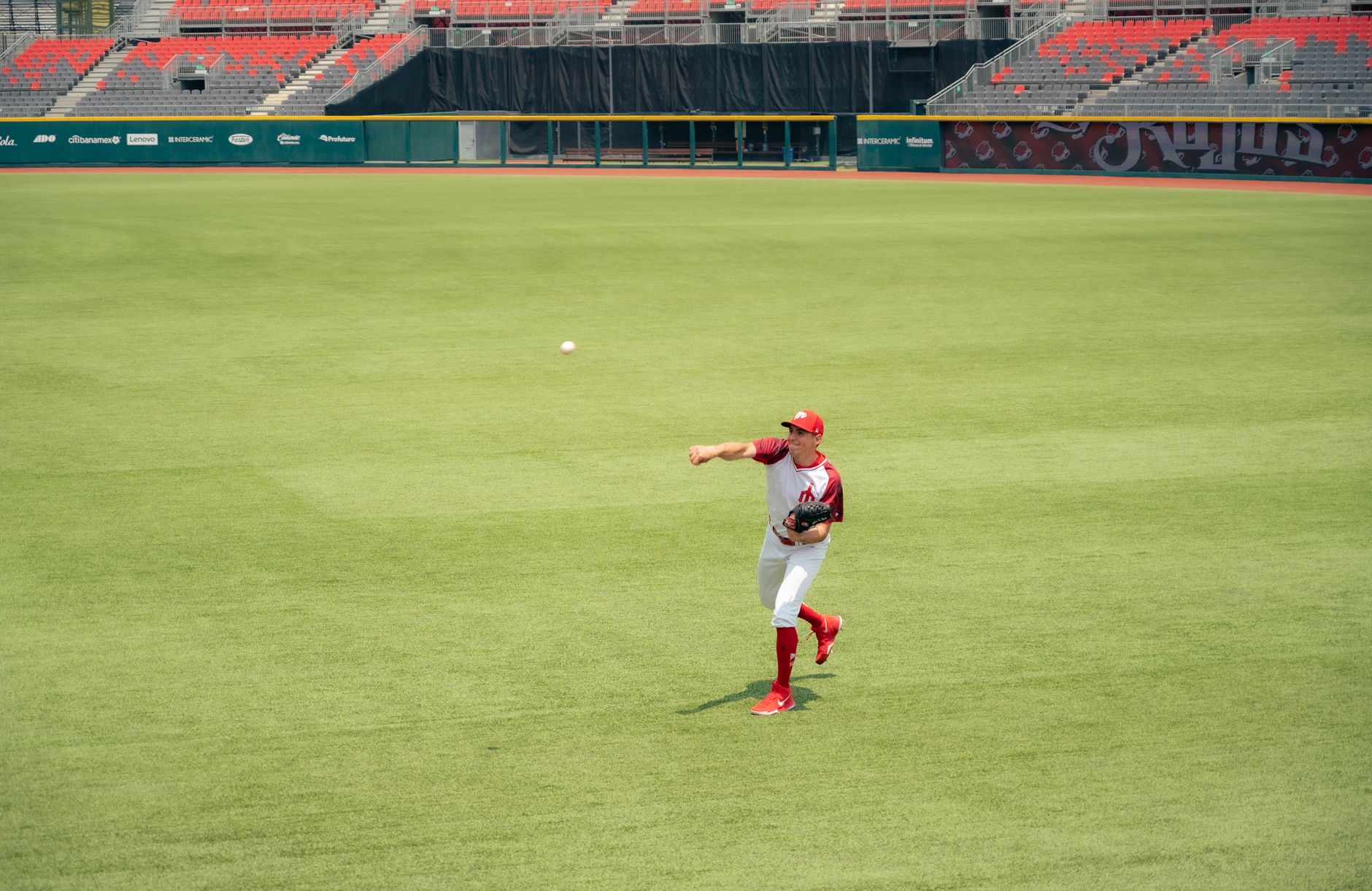 Baseball player throwing ball in a professional stadium wearing a red and white uniform.