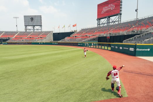 Two baseball players on field with empty bleachers in stadium setting, preparing for game.