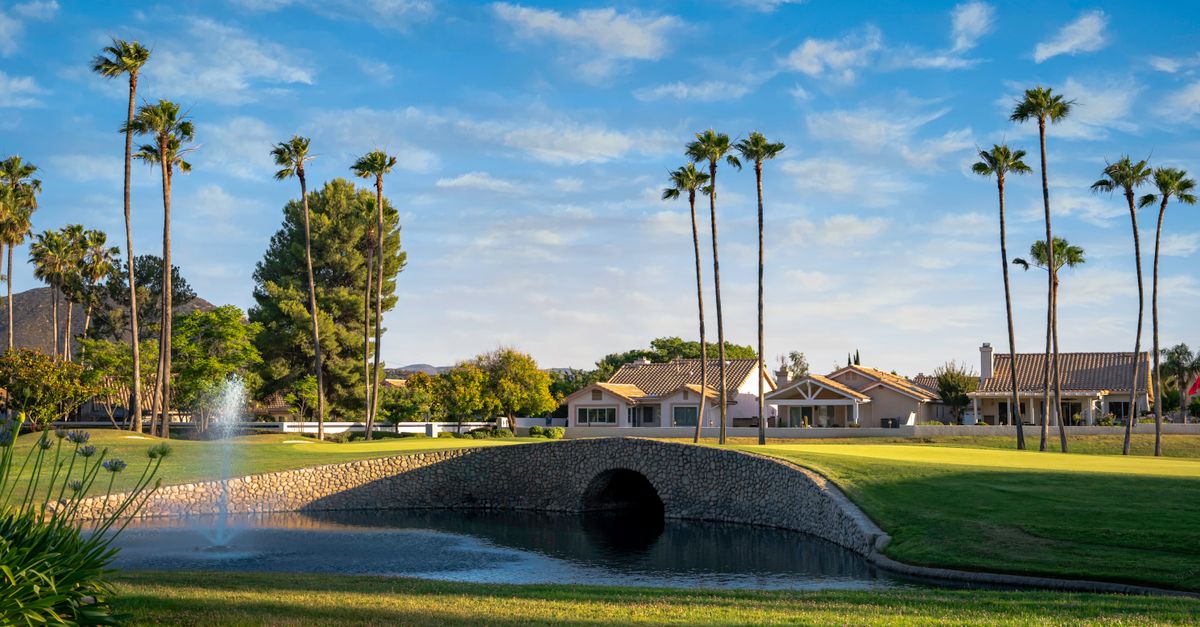 Idyllic scene in Banning, California with a bridge over a pond and palm trees under a clear sky.