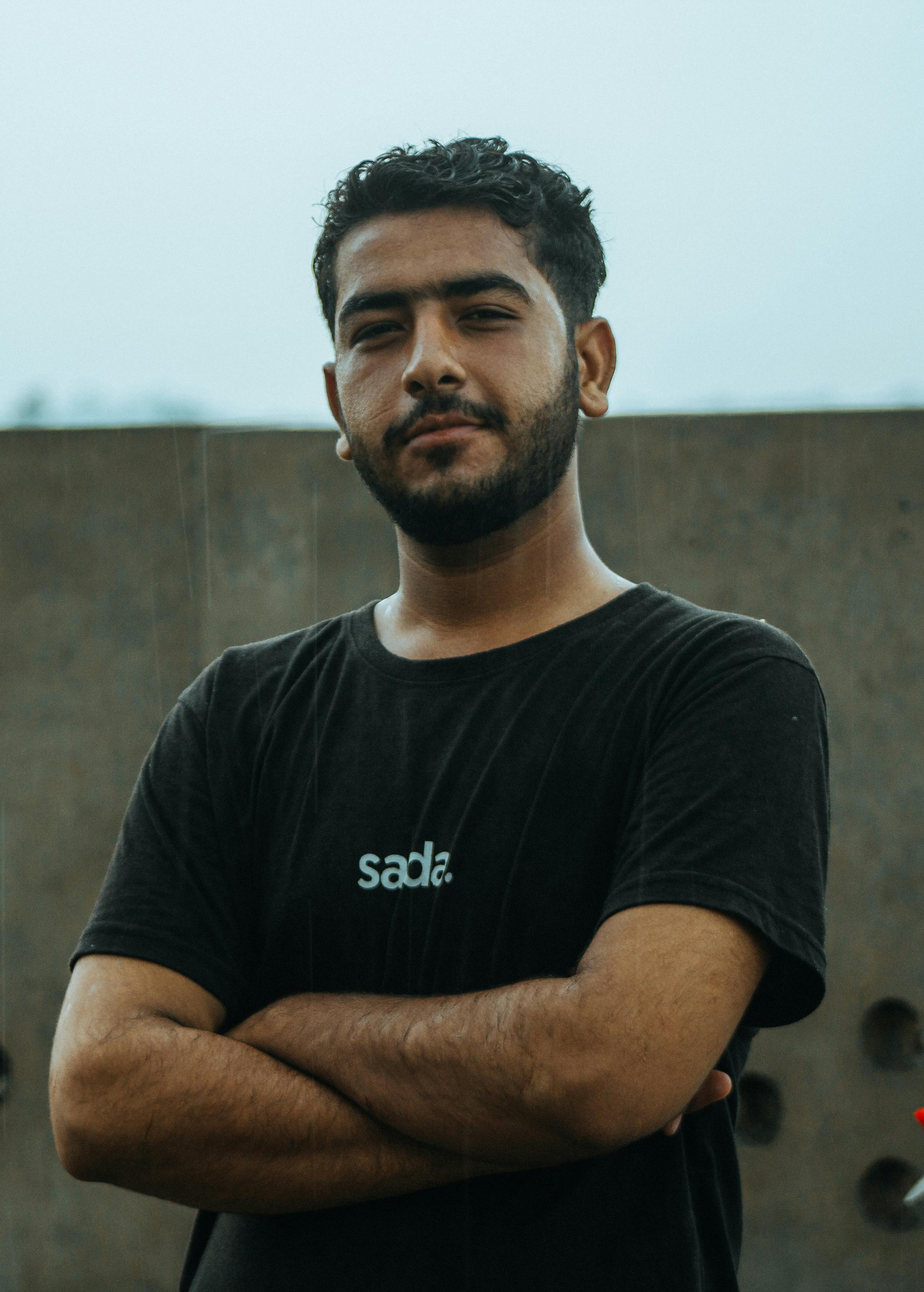 Portrait of a confident young man in a black T-shirt standing with arms crossed outdoors in Rahim Yar Khan, Pakistan.