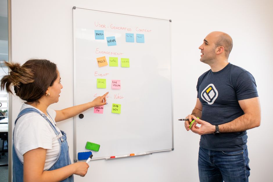 Two colleagues discussing a project plan on a whiteboard in a modern office environment.