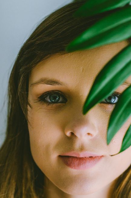 Crop face of calm young woman with blue eyes covered wuth green plant branch