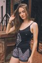 Confident slim female with hand in hair in casual outfit standing against brick building outdoors and looking at camera