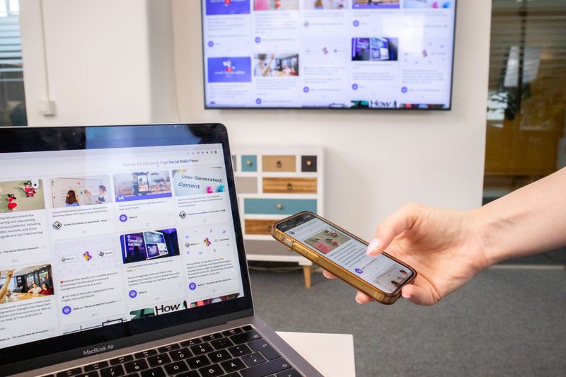 Person using smartphone and laptop in a modern office environment with digital screens.