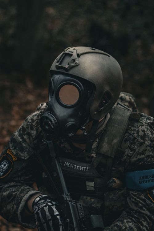 Free A soldier wearing full tactical gear and gas mask, holding a weapon, in a forest setting. Stock Photo