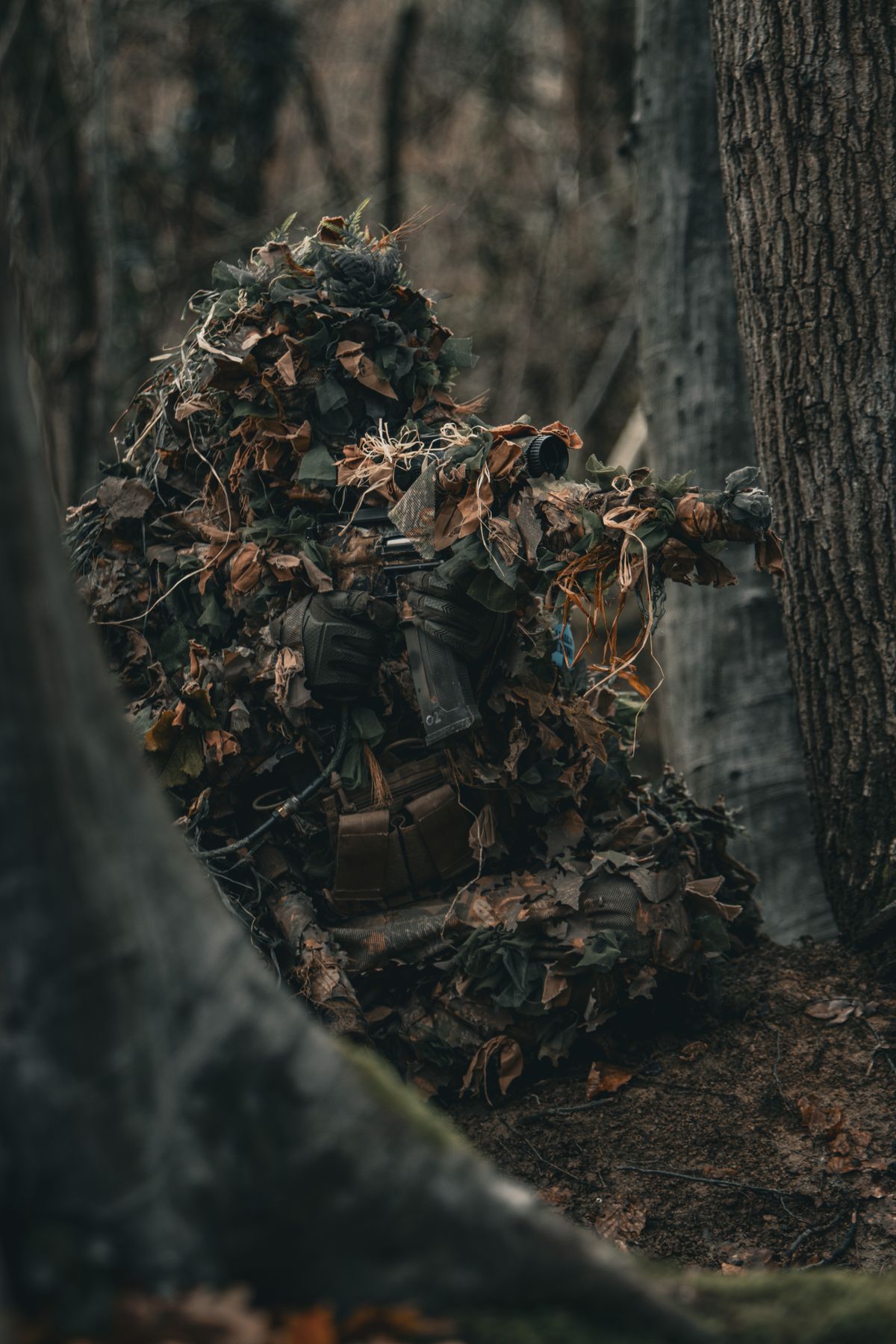 Joueur d'airsoft en tenue ghillie progressant en forêt