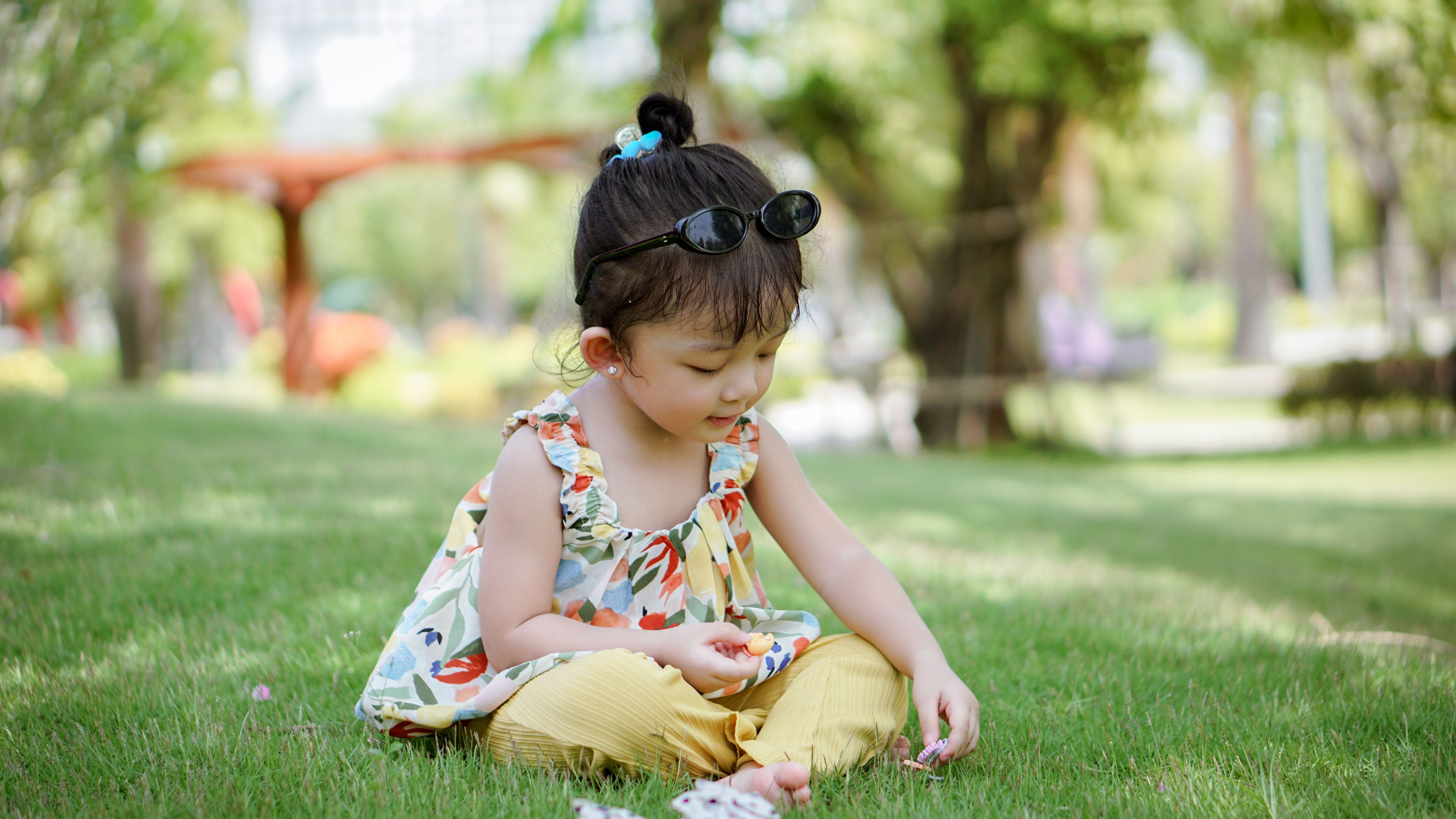A little girl sitting on the grass in the park · Free Stock Photo