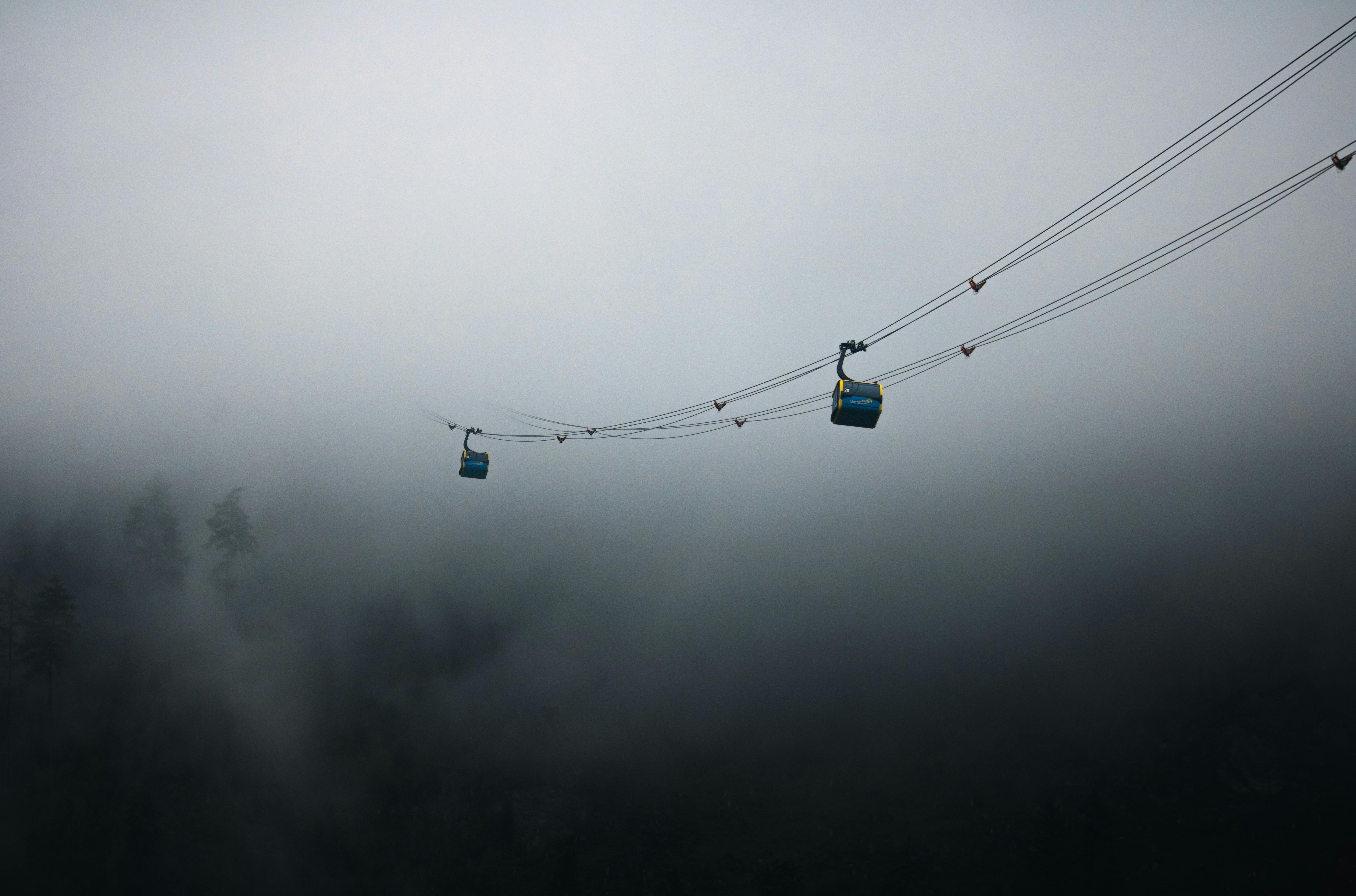 two cable cars are suspended in the fog