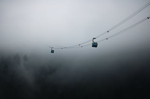 Two cable cars are suspended in the fog