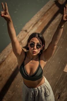 Young woman in sunglasses striking a playful pose by the water. Summer vibes.